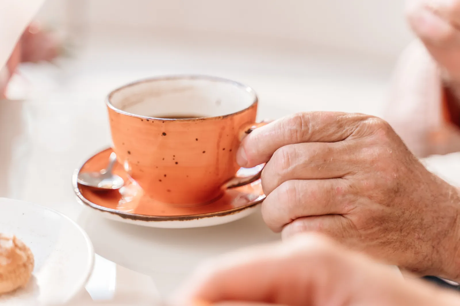 Iäkkään käsi pitelee kahvikuppia pöydän ääressä